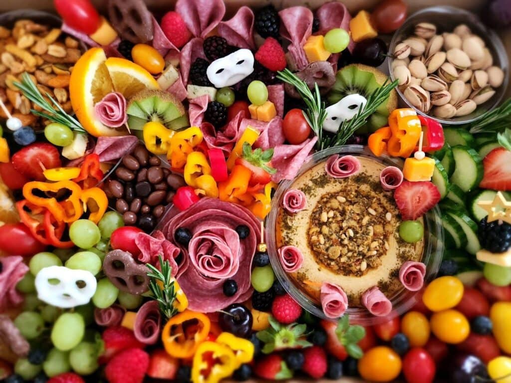 Ripe fruit, nuts, vegetable skewers, cheese, and dips on a festive platter for The Enchanted Event C, featuring colorful fresh produce, assorted snacks, and garnishes ideal for a celebratory gathering or party setting.